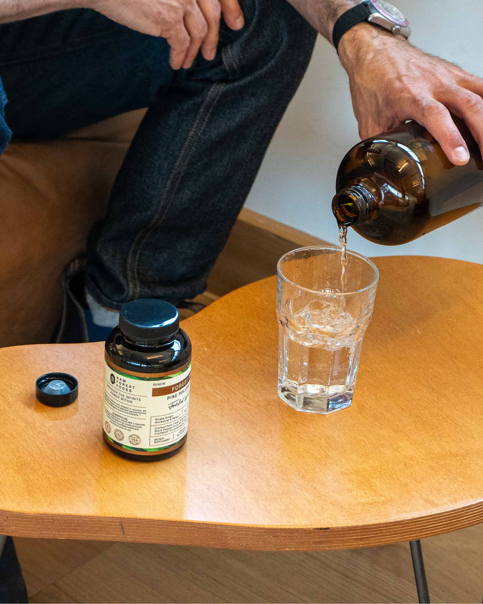 Pouring water into a glass beside supplement bottle