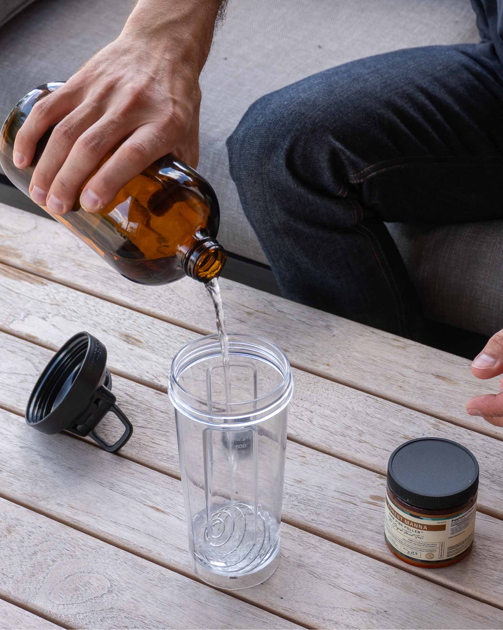 Person holding a glass of water while preparing to add RAW Pine Pollen