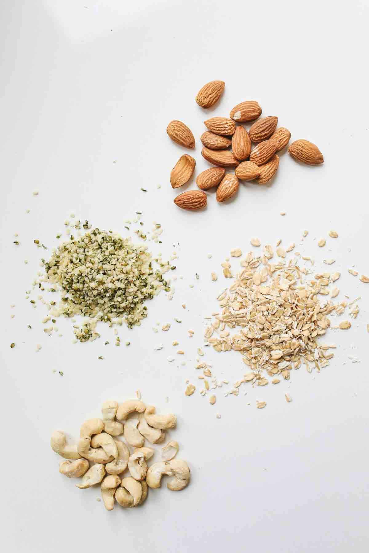 Top-down view of almonds, cashews, hemp seeds, and oats arranged on a white background.