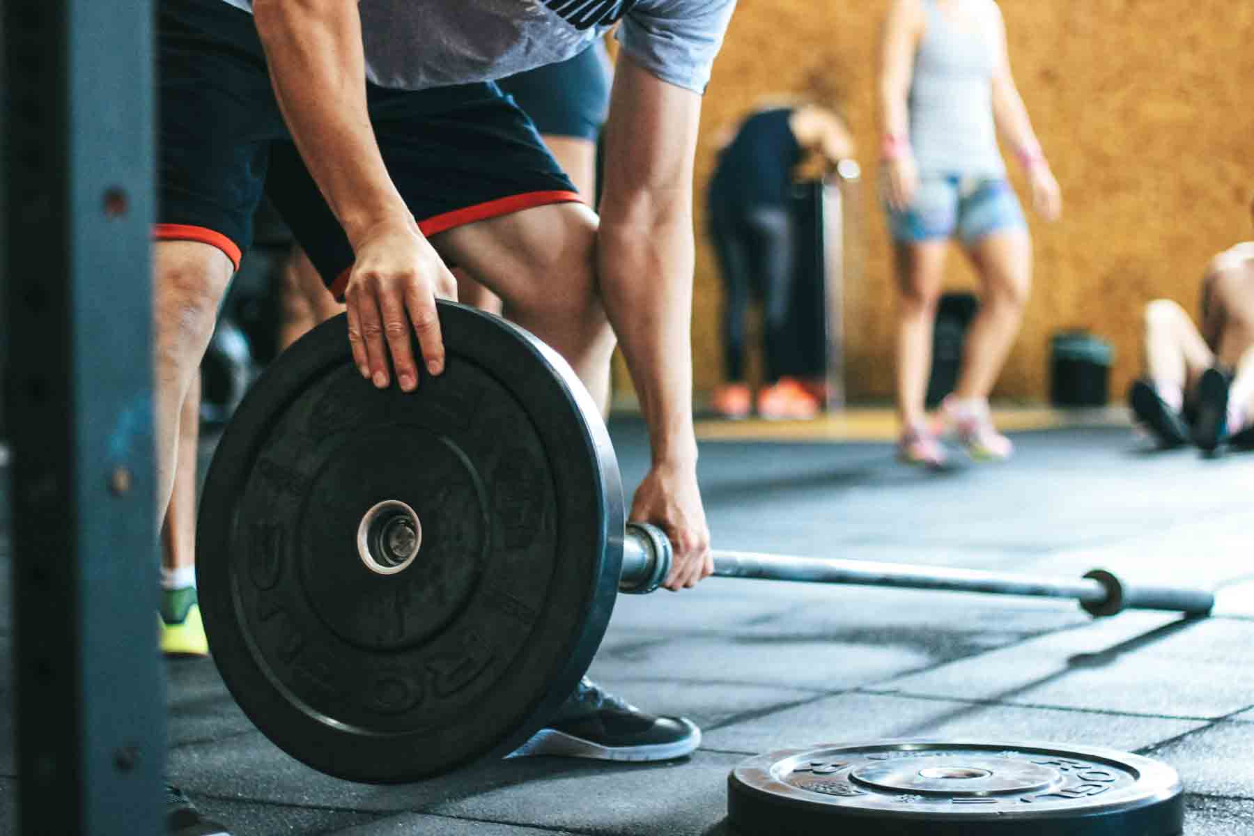 Person preparing to lift a heavy barbell at the gym, with other gym-goers in the background.